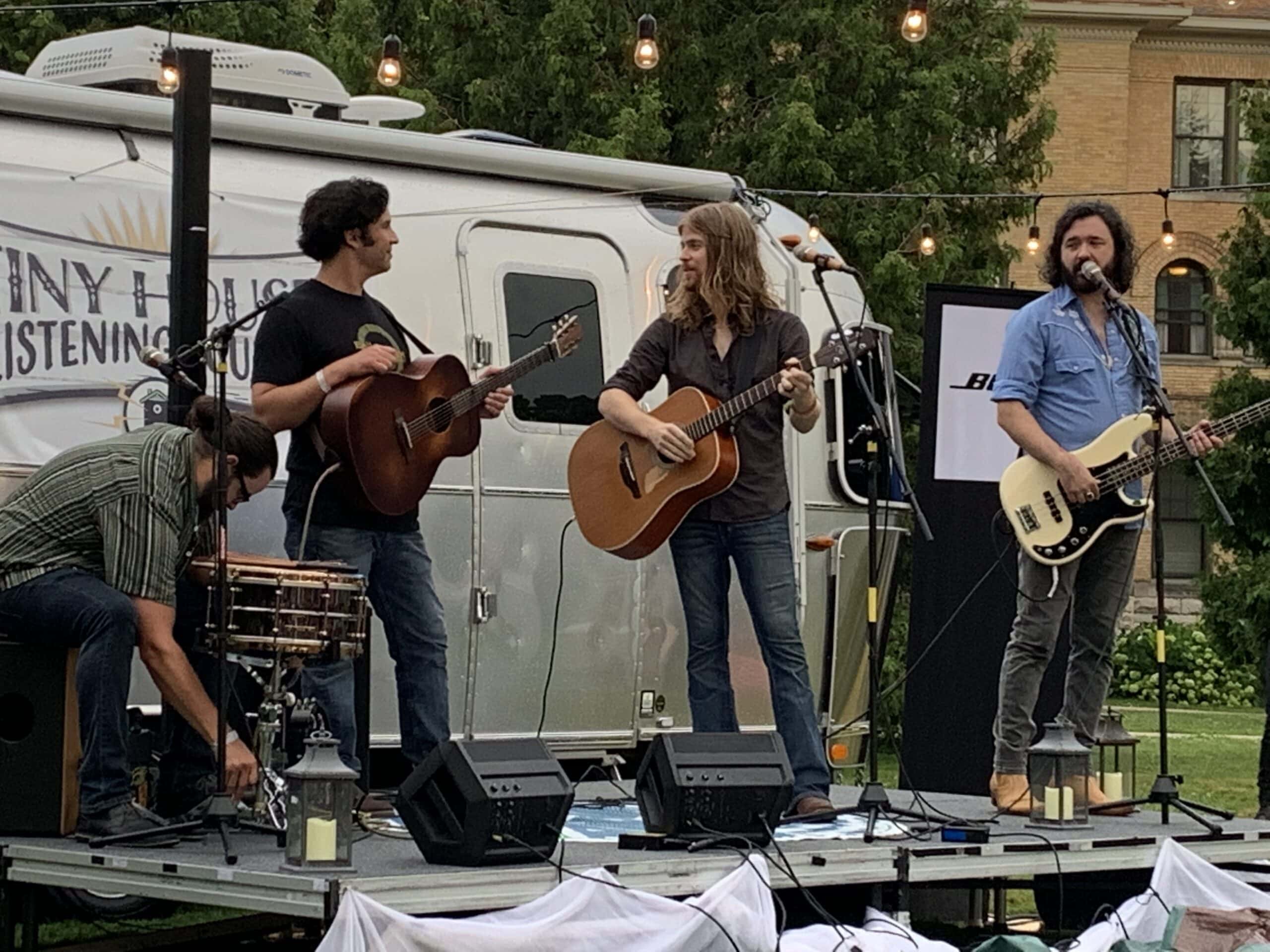 A three piece guitar band playing on an outdoor stage