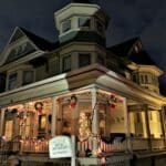 A Victorian home decorated for Christmas is lit up at dusk.