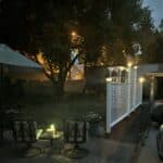 The white lattice fence along the right side of the picture is adorned with glowing solar light caps on the posts. Along with solar lamps on the patio table in the foreground, they enhance the backyard gardens at dusk.