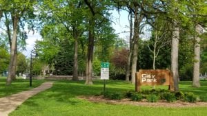 Wooden City Park sign with gold lettering in forefront of picturesque park