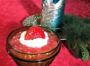 Rhubarb Tapioca pudding in green cut-glass dish with whip cream and a strawberry on top